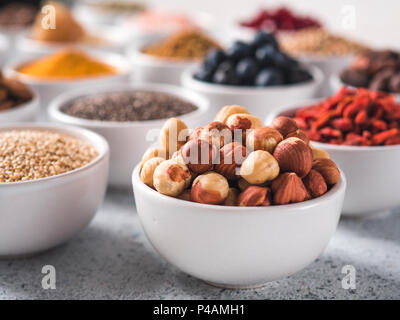 Petit bol blanc en noisette et d'autres de l'air sur l'arrière-plan. Focus sélectif. De l'air différents ingrédients. Concept et illustration pour superfood et detox food Banque D'Images