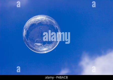 Une bulle de savon irisée flotte dans un superbe ciel bleu. Un coup d'œil à la bulle révèle le reflet du photographe et de City Plaza. Banque D'Images