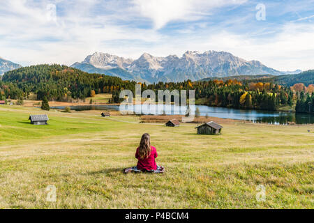 Femme assise et regardant Gerold lac et montagnes des Alpes. Krün, Upper Bavaria, Bavaria, Germany. Banque D'Images