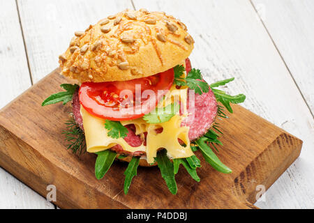 Close up de savoureux hors-d'œuvre de minces tranches de salami épicé sur du pain avec du fromage, tomates et fines herbes sur une planche à découper, l'espace de copie. Banque D'Images