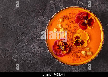 Soupe de carottes / citrouille avec le safran et fleurs comestibles pansy, vue du dessus. Banque D'Images
