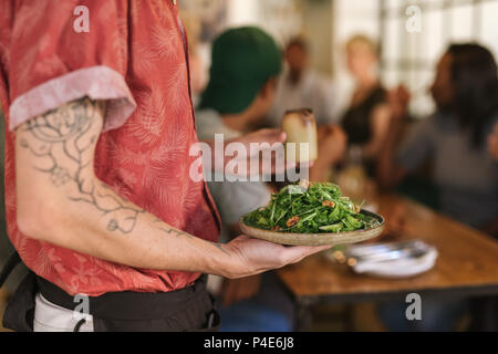 Waiter serving salad de clients assis à une table de restaurant Banque D'Images