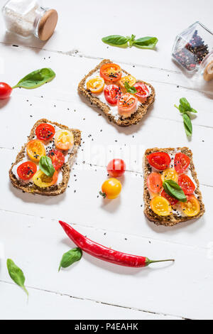 Sandwich au fromage à la crème, tomates cerises et basilic sur table en bois blanc Banque D'Images