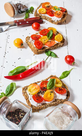 Sandwich au fromage à la crème, tomates cerises et basilic sur table en bois blanc Banque D'Images