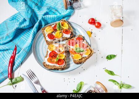 Sandwich au fromage à la crème, tomates cerises et basilic sur table en bois blanc. Banque D'Images