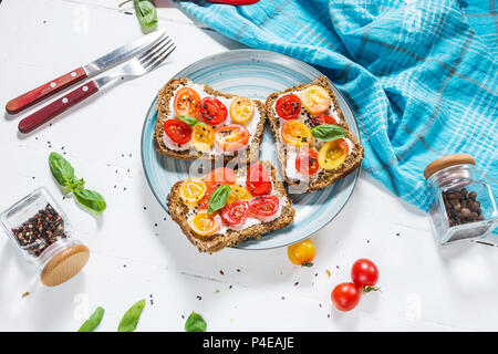 Sandwich au fromage à la crème, tomates cerises et basilic sur table en bois blanc. Banque D'Images