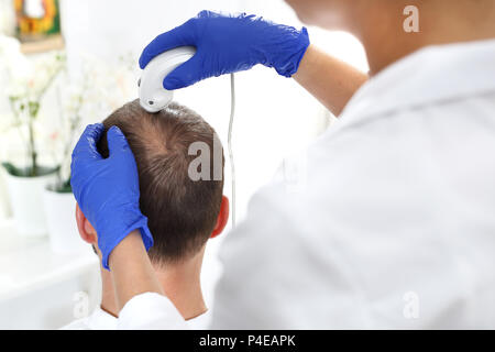 Analyse microscopique de l'état des cheveux et du cuir chevelu. La tête d'un homme dont les cheveux sont effilants pendant l'examen du cuir chevelu Banque D'Images