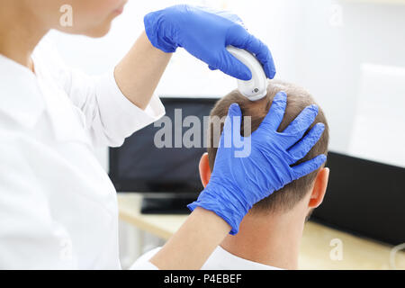 Examen trichologique. Analyse microscopique de l'état des cheveux et du cuir chevelu. La tête d'un homme dont les cheveux sont effilants au cours de l'examen Banque D'Images