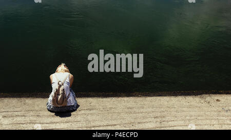 Cheveux blonds femme assise par l'eau de la rivière sombre, triste, déprimé et seul, pleurer Banque D'Images