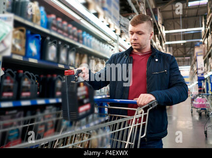 Homme avec un panier dans le magasin choisit l'huile voiture Banque D'Images