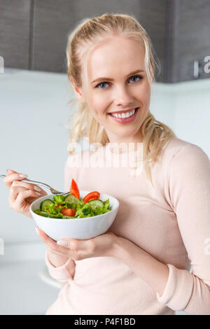 Belle fille blonde holding bowl avec une salade de légumes frais et smiling at camera Banque D'Images