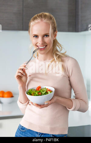 Belle fille blonde de manger une salade de légumes et smiling at camera Banque D'Images