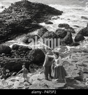 Années 1950, historique, la mère, le père et leur jeune garçon sur le rock hexagonal à colonnes le célèbre Giant's Causeway, le comté d'Antrim, en Irlande du Nord. Cette zone côtière unique de colonnes de basalte, le résultat d'une ancienne fissure volcanique éruption est une merveille de la nature. Banque D'Images