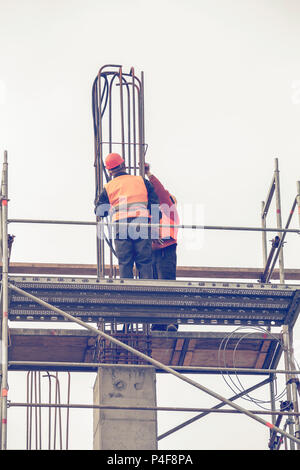 Les travailleurs sur la plate-forme d'échafaudage lié d'armature et de barres d'acier, pilier en béton en construction. Vintage style. Banque D'Images