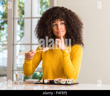 African American Woman eating sushi à l'aide de baguettes à la maison visage sérieux de penser à question, idée très confus Banque D'Images