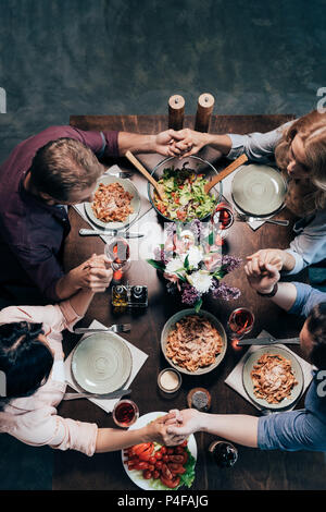 Vue de dessus de la main d'amis d'âge moyen en priant avant le dîner Banque D'Images