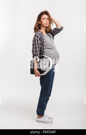 Contrarié pregnant woman holding échelles et looking at camera isolated on white Banque D'Images