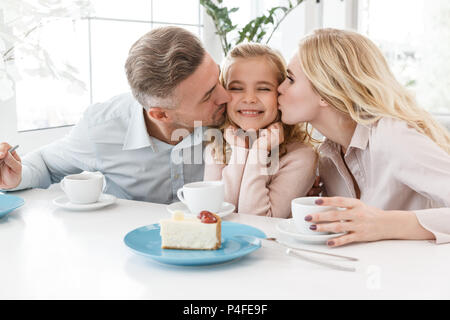 Les parents embrassant leurs heureux petite fille tout en passant du temps dans cafe Banque D'Images