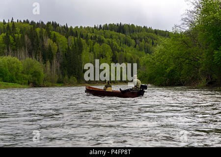 Deux personnes dans un bateau à fond plat en bois avec moteur hors-bord flotter le long de la rivière à l'état sauvage sur un jour nuageux Banque D'Images