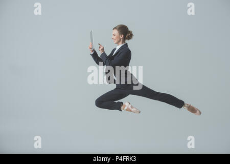 Businesswoman in suit et chaussures de ballet et de saut à l'aide de tablette numérique, isolé sur gris Banque D'Images