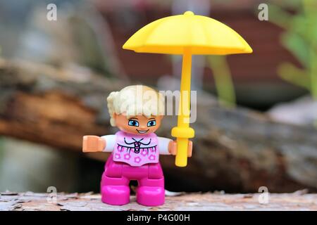 Duplo girl holding a caractère parapluie jaune contre un arrière-plan flou - News Concept Banque D'Images