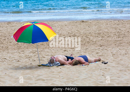 Bournemouth, Dorset, UK. 22 juin 2018. Météo France : belle chaude journée ensoleillée à plages de Bournemouth en tant que visiteurs, chef de la station pour profiter du soleil, comme la prévision est pour les températures d'augmenter. D'âge mûr en train de bronzer sur une plage avec parasol coloré. Credit : Carolyn Jenkins/Alamy Live News Banque D'Images