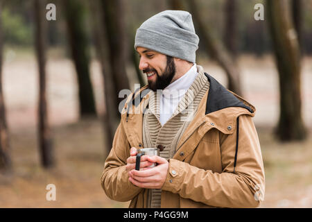 Bel homme heureux avec tasse de boisson chaude dans la forêt Banque D'Images