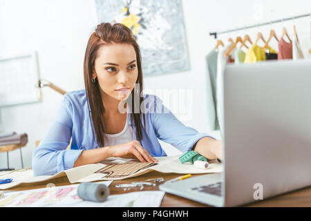 Couturière sérieuse looking at laptop à la table de travail Banque D'Images