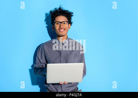 Young African American boy holding laptop sur fond bleu Banque D'Images
