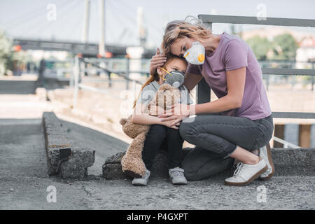 Mère et fille dans des masques de protection hugging on street, la pollution de l'air concept Banque D'Images