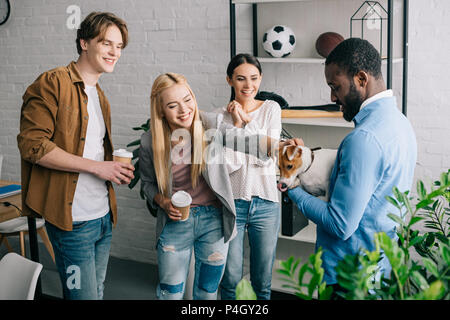 African American businessman holding dog entouré de collègues souriants avec les tasses de café Banque D'Images