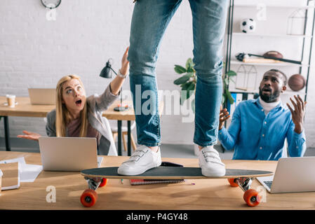 Portrait of businessman riding sur longboard sur table et choqué collègues de bureau moderne Banque D'Images