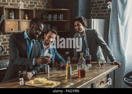 Male amis en costumes en utilisant smartphone et de boire de l'alcool pendant la fête à la maison Banque D'Images