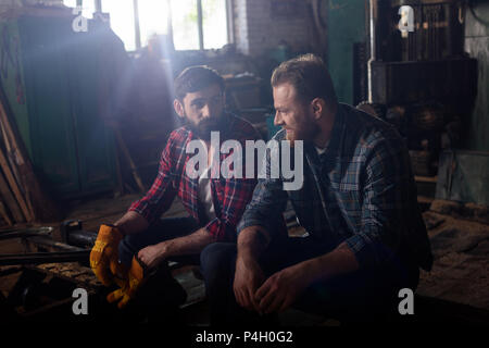 Deux travailleurs barbu assis et de parler les uns aux autres à sawmill Banque D'Images