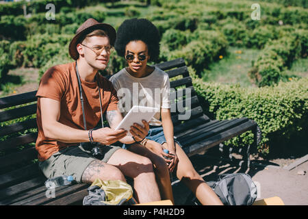 Couple multiethnique de jeunes touristes assis sur un banc avec tablette numérique Banque D'Images