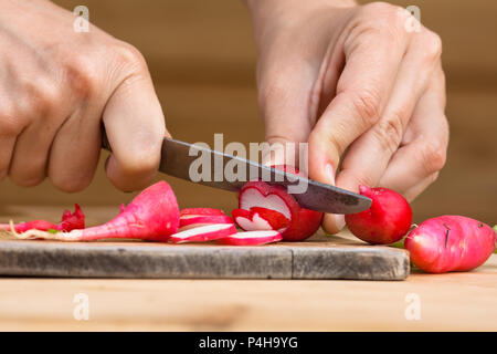 Mains de woman slicing radis frais sur la planche à découper en bois Banque D'Images