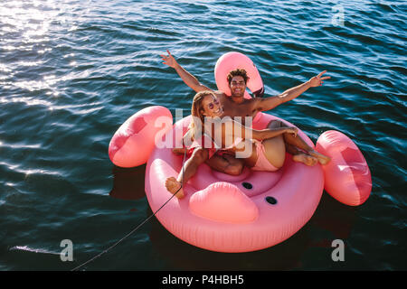 Beau couple enjoying inflatable toy ride derrière un bateau dans la mer. L'homme et la femme assis sur un jouet gonflable lié à un bateau en mer. Banque D'Images