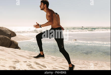 Man doing fitness workout sur une plage sur une journée ensoleillée. Vue latérale d'un homme athlétique s'exécutant sur la plage. Banque D'Images