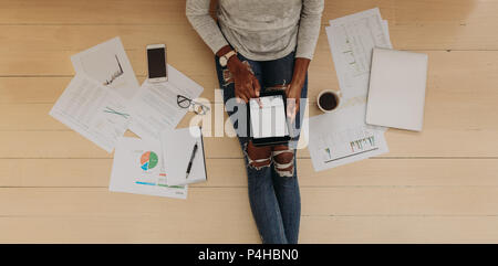 Vue de dessus d'une femme entrepreneur dans le quartier branché de jeans sur tablet pc à la maison. Femme assise sur le plancher à la maison à l'aide d'un tablet pc avec coff Banque D'Images