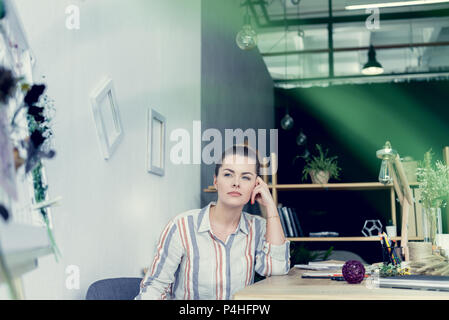 Pensive attractive businesswoman sitting at table in modern office Banque D'Images