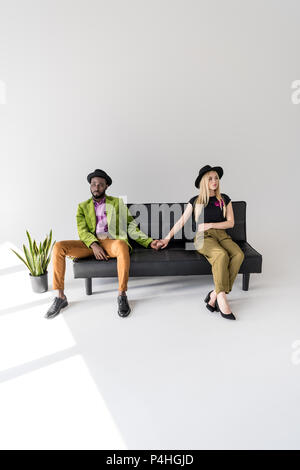 Young couple holding hands multiethnique tout en étant assis sur la table et à l'écart sur gris Banque D'Images