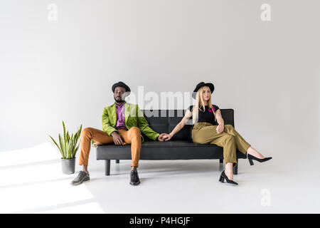 Jeune élégant couple multiethnique, assis sur un canapé et à l'écart sur gris Banque D'Images