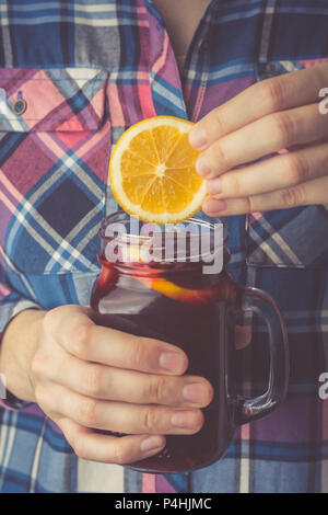 Une jeune femme dans une chemise est titulaire d'une tasse de vin chaud fait maison dans ses mains, plonge une tranche de citron dans une tasse. Photo couleur Banque D'Images