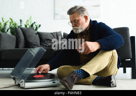 Man élégant mettre lunettes vinyl record en couronne en position assise sur un tapis Banque D'Images