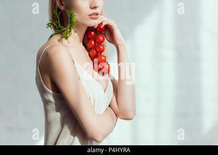 Vue partielle de la femme avec des tomates cerises dans la main et d'oreille faites de roquette fraîche, concept de vie végétalien Banque D'Images