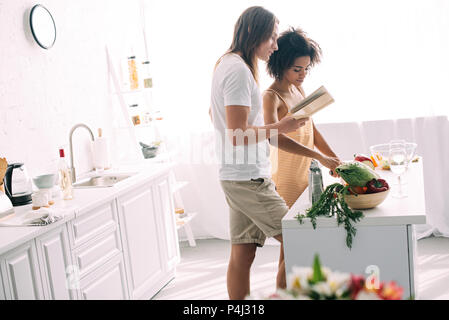 Vue latérale du jeune couple multiethnique et à la recette de cuisine au livre Banque D'Images