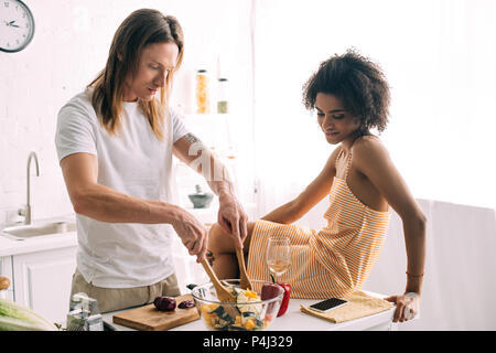 African American woman petit ami pendant qu'il cuisine salade à la cuisine Banque D'Images