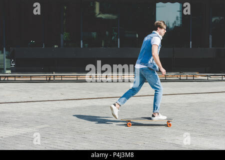 Vue latérale du jeune skateur professionnel équitation longboard par street Banque D'Images