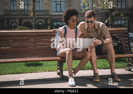 Couple multiethnique de jeunes touristes à la recherche de la carte et l'assis sur un banc Banque D'Images