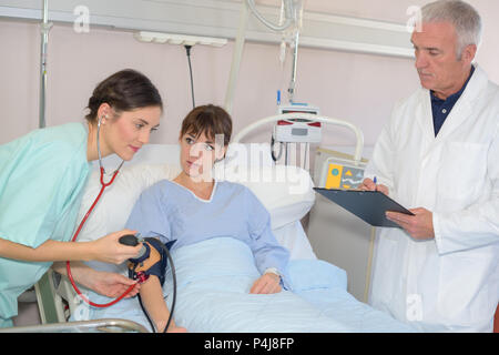 Infirmière de prendre la tension artérielle de female patient in hospital bed Banque D'Images